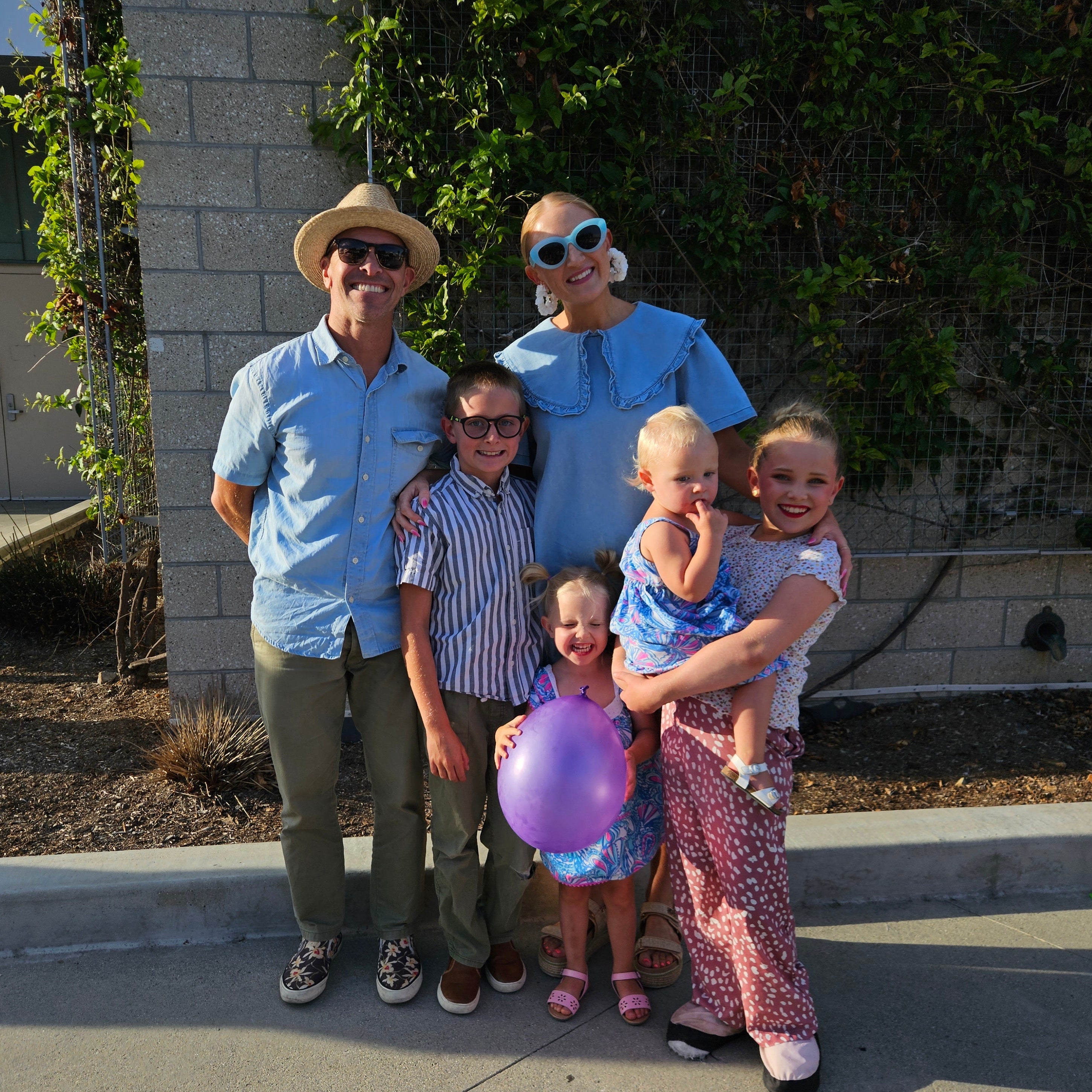 Family of six posing outdoors with a purple balloon